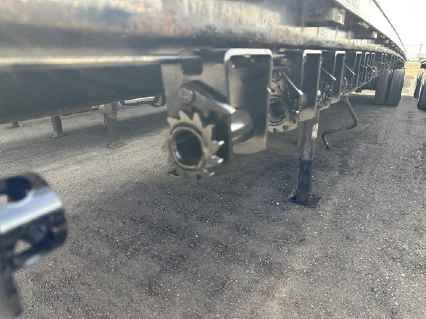 Trailer undercarriage showing bolted mounting brackets and circular pin housing on a 2015 Manac 48' steel flatbed.