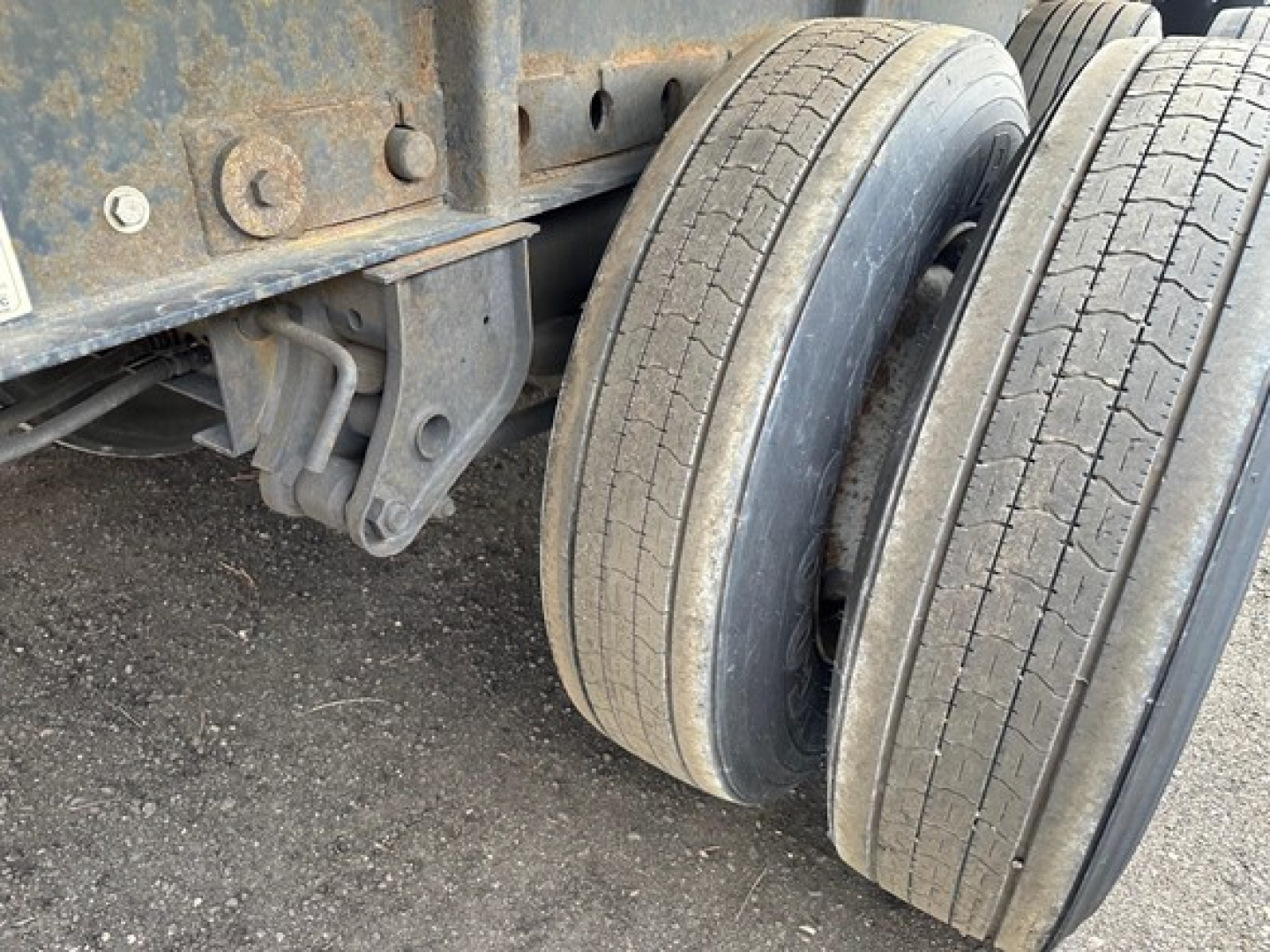 Trailer axle showing dual tires mounted on a Manac flatbed trailer with steel frame and suspension components visible