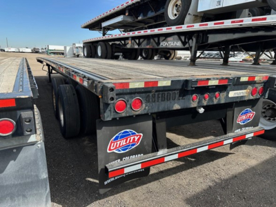 Flatbed trailer rear view showing steel deck, red taillights, reflective tape, and Utility brand mudflaps on a 2015 Manac 48' steel flatbed.