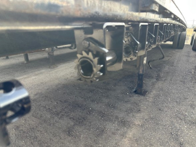 Flatbed trailer underside showing connectors and landing gear leg with mounting hardware and alphanumeric cup-like hitch point