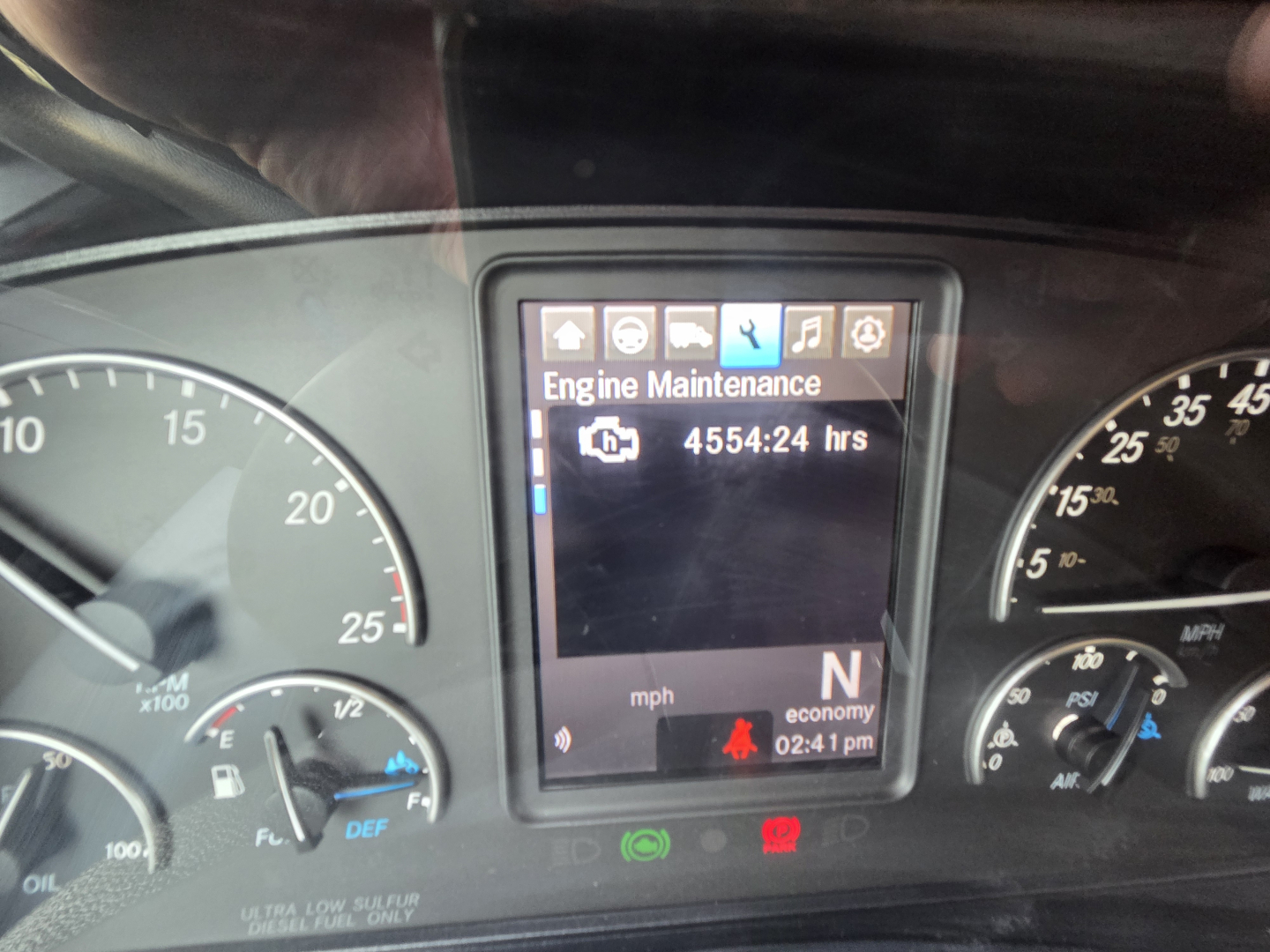 Dashboard display showing Engine Maintenance screen with 4554.24 hrs on a Freightliner cab truck; gauges visible on either side.