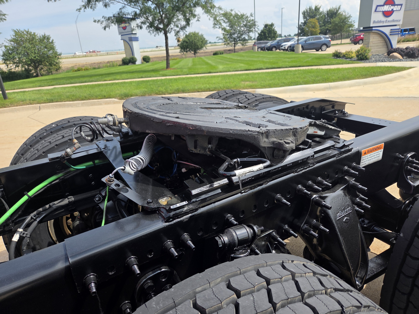 Truck chassis showing fifth wheel mounting area and cabless frame with dual rear wheels and various hoses; metal components and drivetrain visible.
