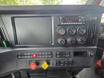 Dashboard panel of a Freightliner PT126064S daycab showing steering controls, gauges, climate controls, and a screen; visible knobs, switches, and warning buttons.