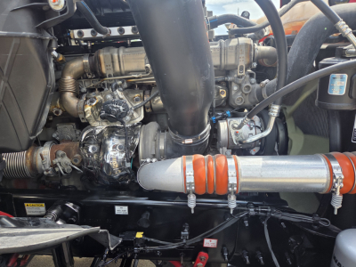 Engine bay of Freightliner PT126064S showing large intake hose, turbocharger, metal piping with orange insulated section, and various metallic engine components.