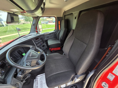 Truck cab interior showing steering wheel, dashboard, and two front seats in a Freightliner sleeper/Day Cab. Visible controls and instrument cluster. No additional text readable.
