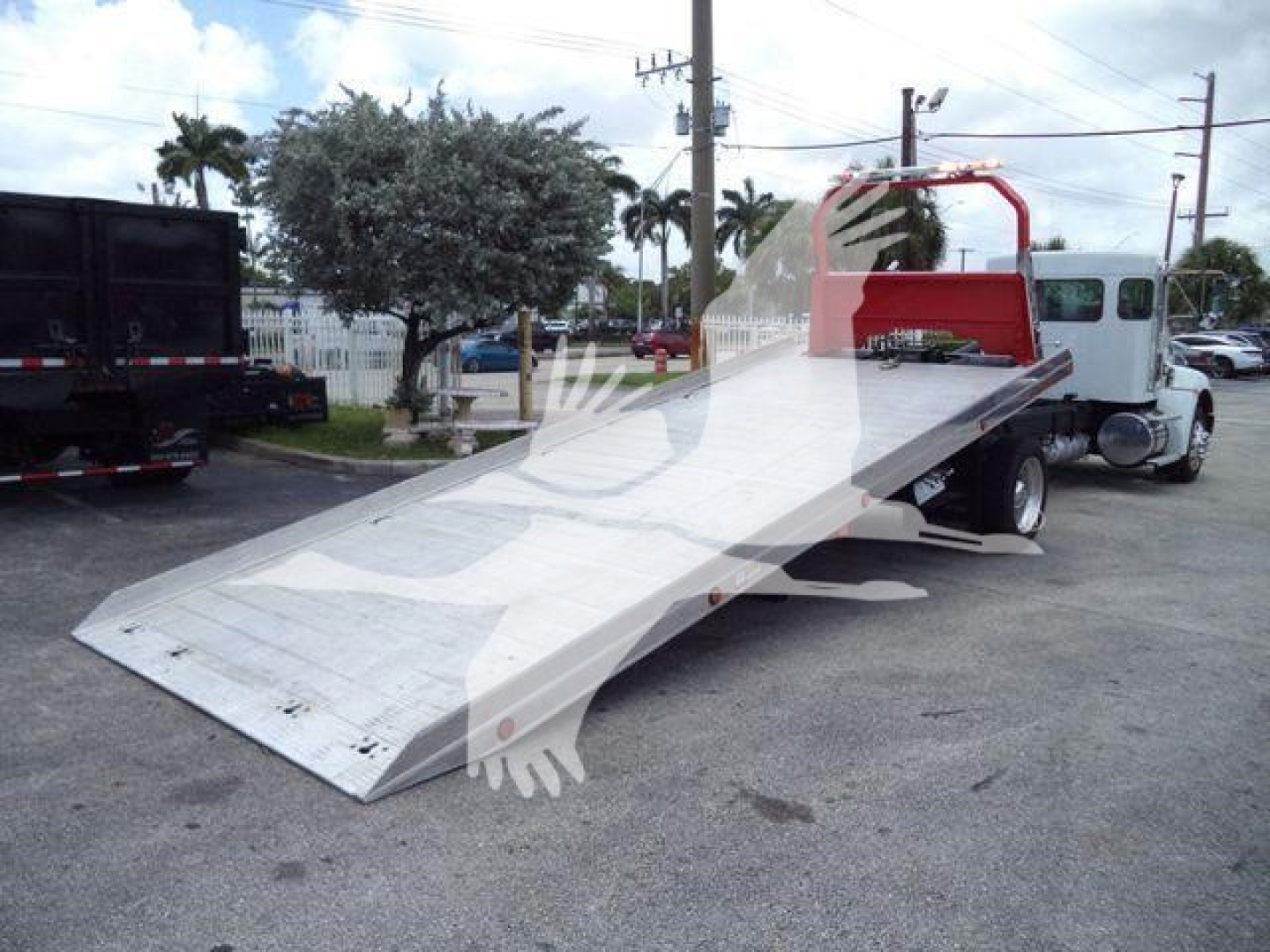 Kenworth T270 rollback tow truck with a lowered flatbed, side view showing the metal ramp and red rollover guard, white cab, tires and utility area.
