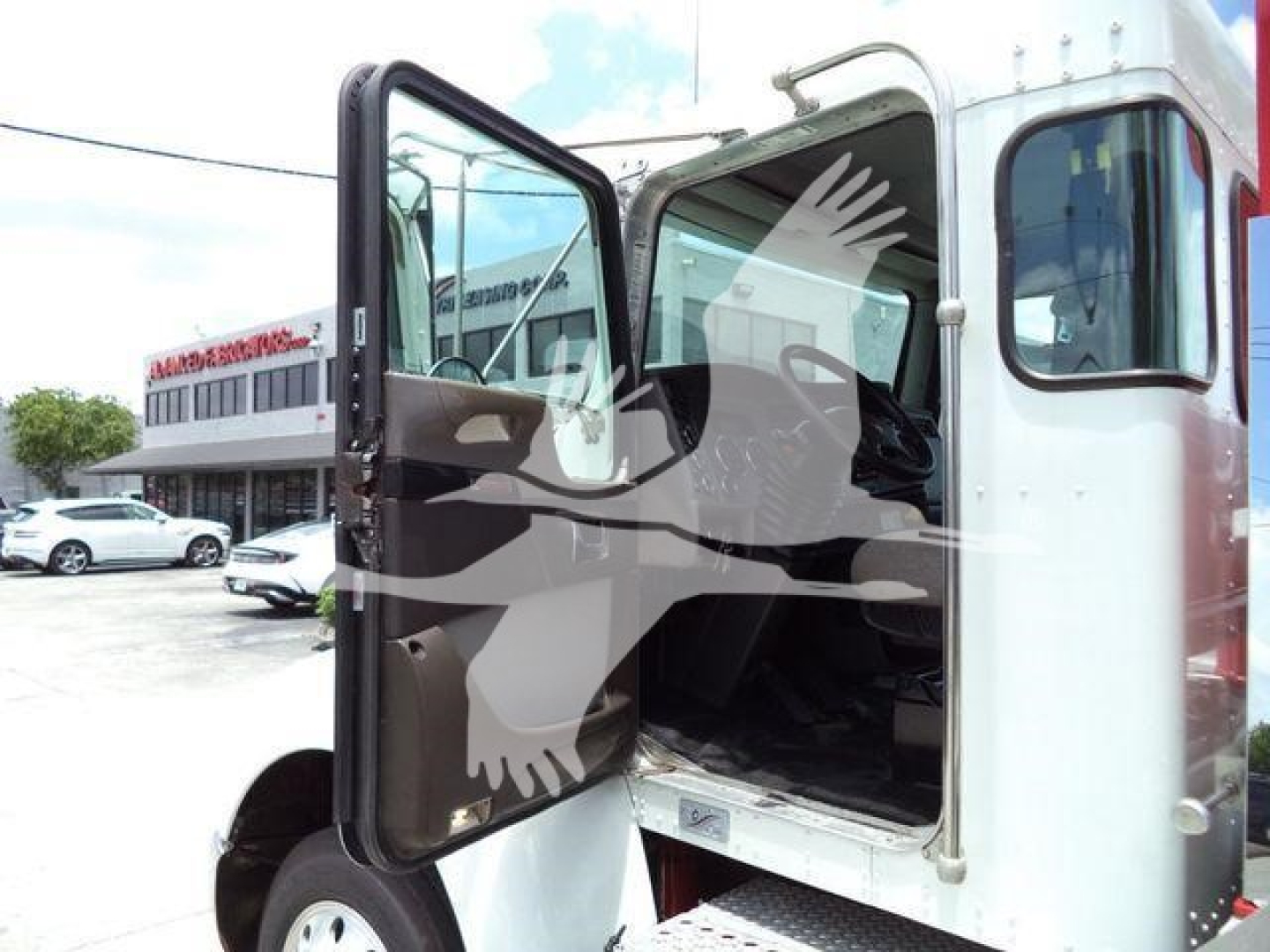 Kenworth truck cab with open driver door showing interior steps, side mirror and doorway.