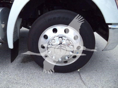Wheel of a Kenworth truck with chrome hubcap and black tire, front fender and part of suspension visible.