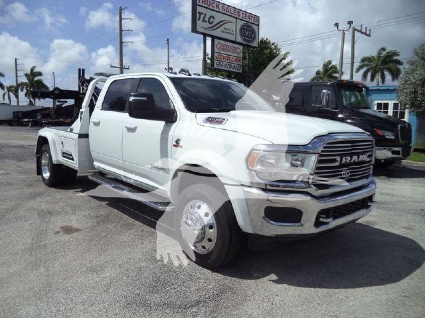 Ram 5500 Laramie truck in a dealership lot, white crew cab with dual rear wheels, chrome front grille. Visible signage in background and a large RAM badge on the grille.