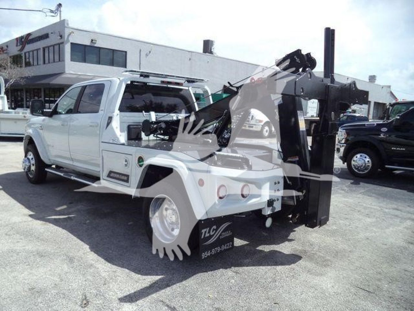Ram 5500 Laramie with heavy-duty winch/service body and black hydraulic crane in a dealer lot, side view showing white cab and equipment rack.
