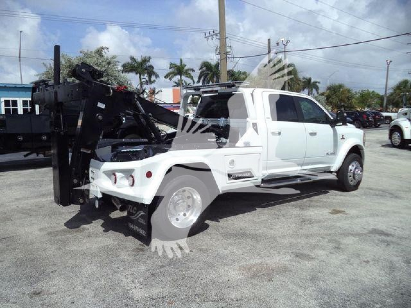 Ram 5500 tow truck with winch apparatus in rear, side view of white pickup with over-mounted winch and carrier; no legible serials or brands visible on side.