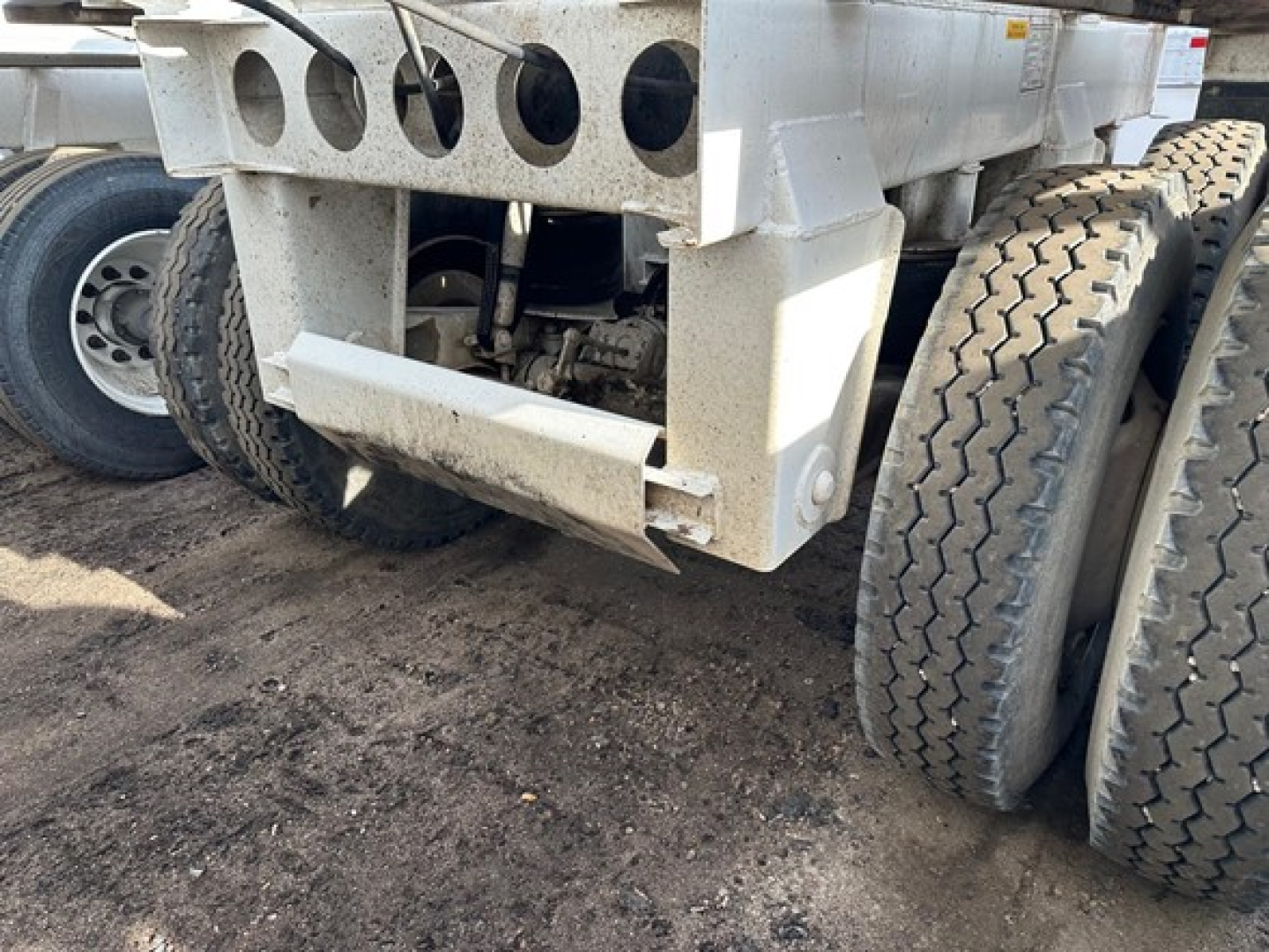 Dump trailer undercarriage showing dual rear axles with large off-road tires and chassis components; visible are the lower frame, suspension linkage, and mounting brackets.