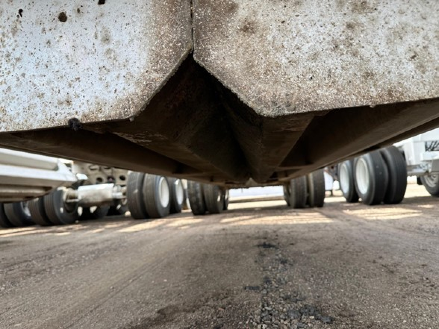 Underside view of a worn dump trailer showing the V-shaped crossmember and dirt/grime on metal surface.