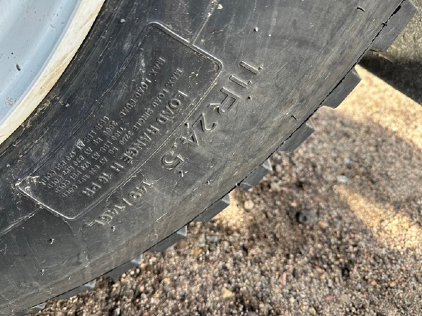 Tire sidewall showing raised lettering: "TIRES 12.5 L  H" and other details, with gravel ground nearby.
