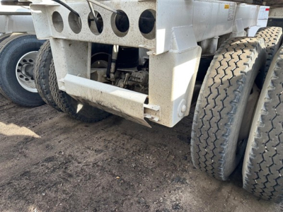 Dump trailer undercarriage showing dual rear axles with large off-road tires and chassis components; visible are the lower frame, suspension linkage, and mounting brackets.