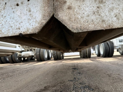 Underside view of a worn dump trailer showing the V-shaped crossmember and dirt/grime on metal surface.