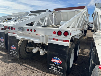 Dump trailer showing rear view with dual axles and white lattice framework, red taillights, and mud flaps labeled Utility Denver Colorado; license plate visible.