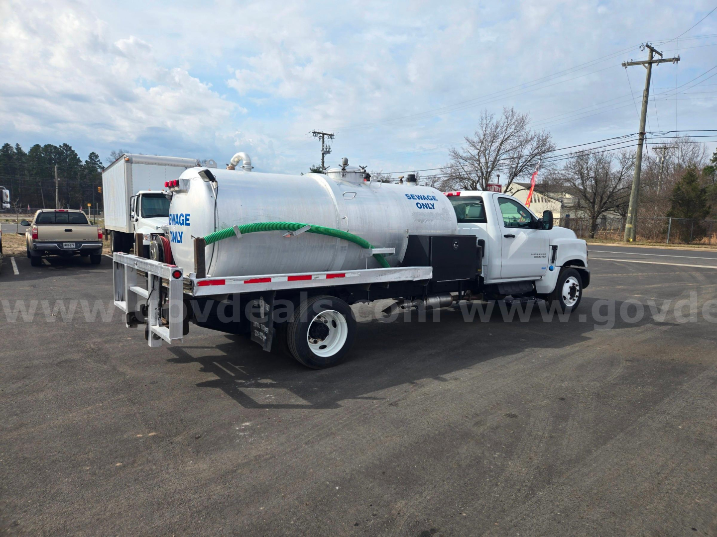 Chevrolet 5500 vacuum truck side/back view with cylindrical tank, green hose, and white cab. visible text includes company markings and equipment labels on the tank.