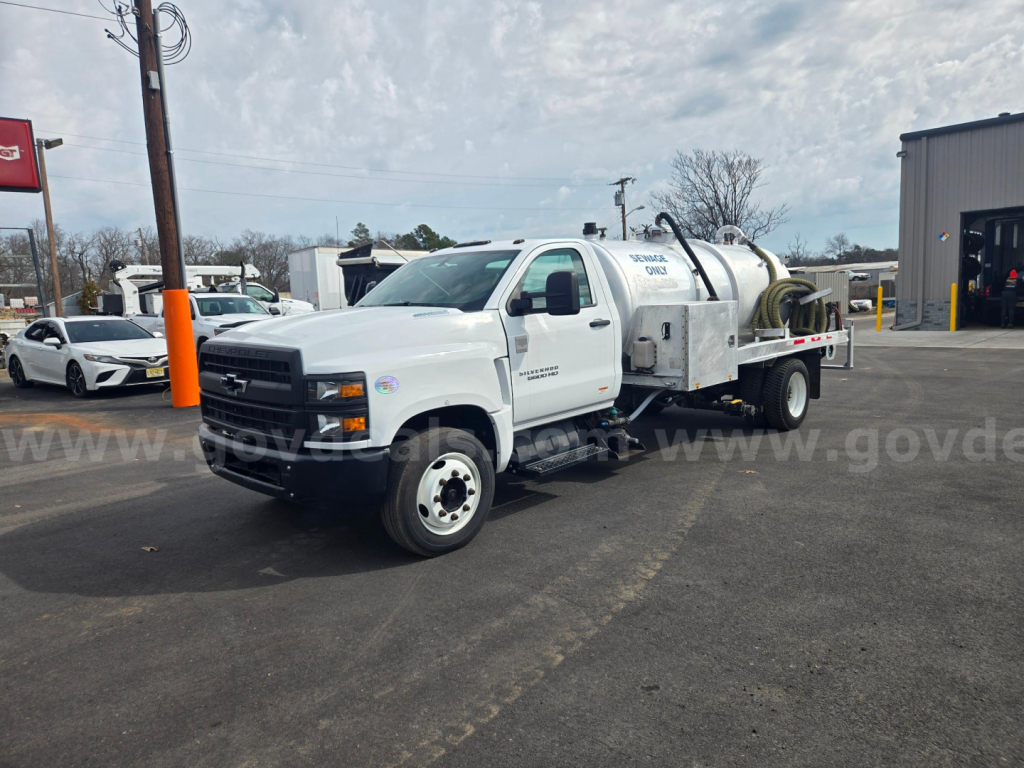 Truck with mounted vacuum tanker showing white cab and tank trailer, Chevrolet logo on grille, serving utility work. Side text and equipment visible.