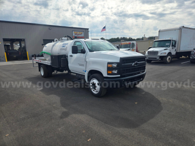 Front-left view of a white 2023 Chevrolet 5500 vacuum truck with a mounted tank and hose reel in a dealership lot.