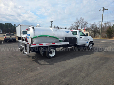 Chevrolet 5500 vacuum truck side/back view with cylindrical tank, green hose, and white cab. visible text includes company markings and equipment labels on the tank.