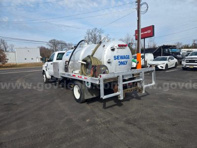 Vacuum truck rear view showing tank labeled SEWAGE ONLY and backhoe hose reel on a white utility chassis.