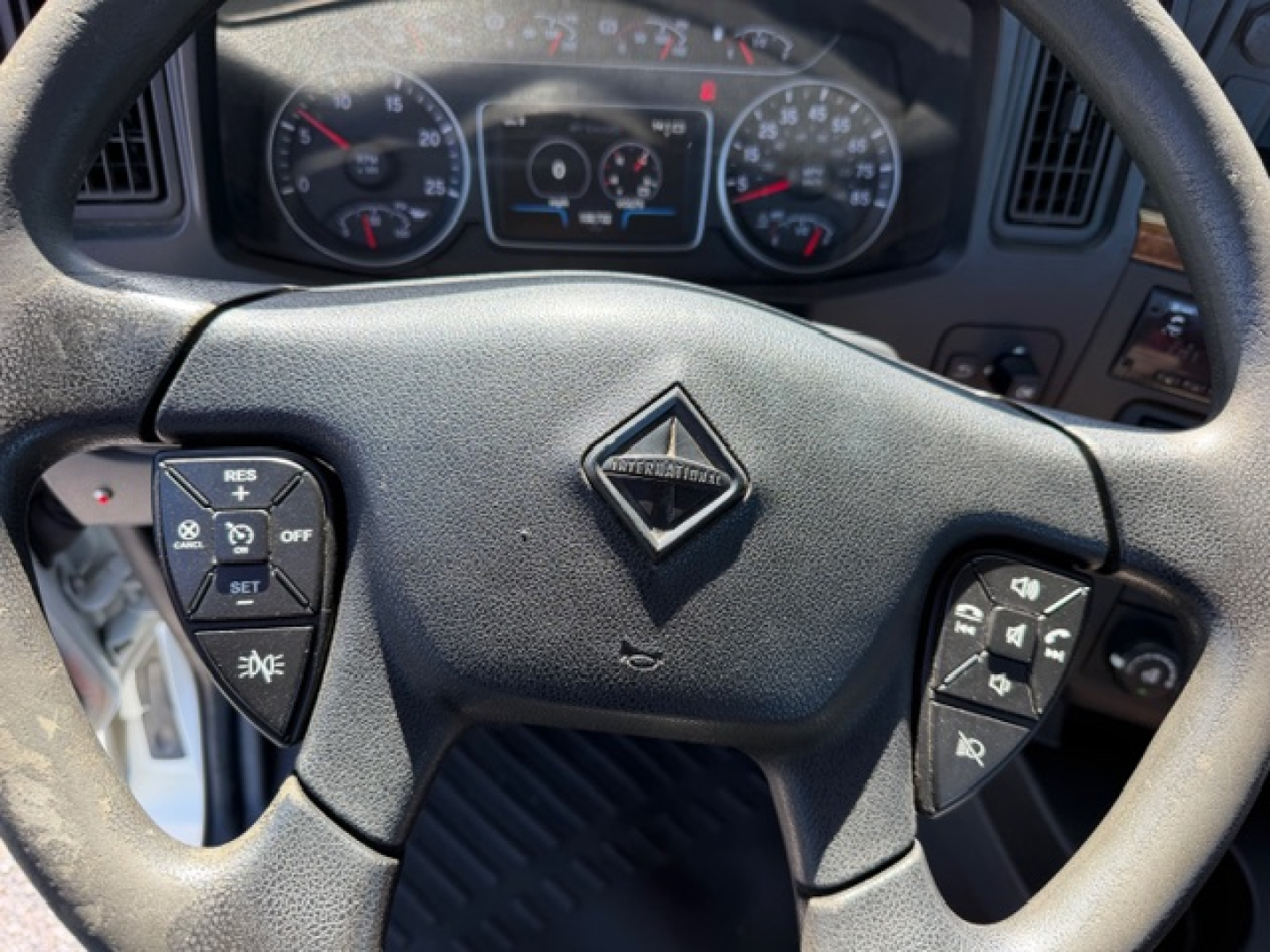 Steering wheel view of a 2018 International LT625 cab truck showing Dodge-like diamond logo center, instrument cluster in background, steering wheel controls on both sides.