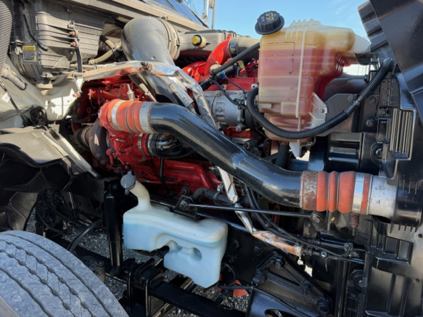 Engine bay of a 2018 International LT625 daytime view showing coolant reservoir, air intake hose, and various hoses and components.