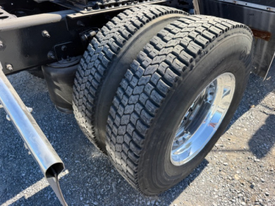 Dual rear wheels on a truck with visible heavy-duty tires and chrome rims; part of the suspension and frame is visible.