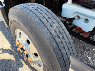Front wheel and tire of a 2018 International LT625 conventional daycab showing tread pattern and wheel with rusted lug nuts, nearby coolant reservoir.
