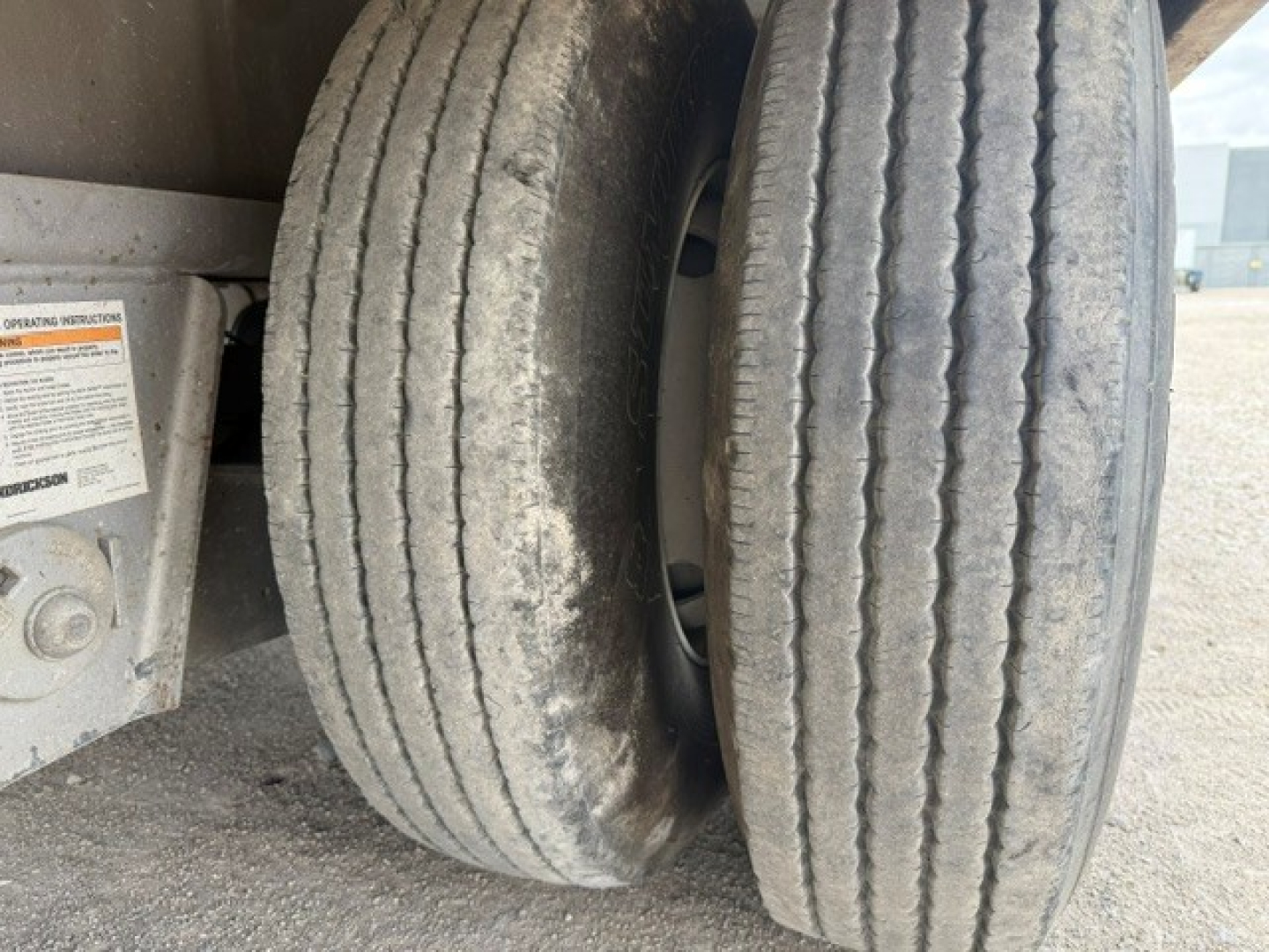 Trailer axle showing dual wheels with tread wear and dirt; partial sticker with operation label nearby.