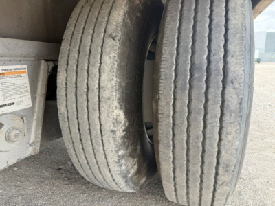 Trailer axle showing dual wheels with tread wear and dirt; partial sticker with operation label nearby.
