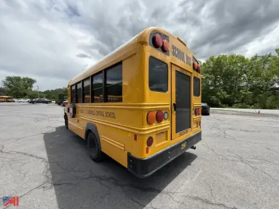 School bus rear and left side view showing yellow body with 'SCHOOL BUS' signage, black bumper, and rear doors; appears in a parking lot.