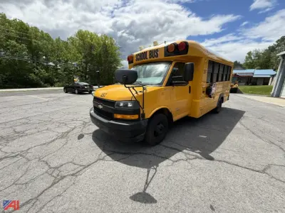 School bus front-left view showing bright yellow body, 'SCHOOL BUS' signage on roof, black bumper, and side windows.