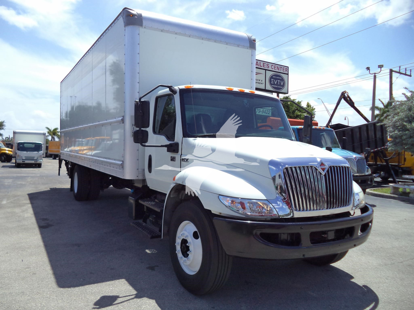 International MV box truck in a dealership lot, white cab with large chrome grille, box body, front left view.