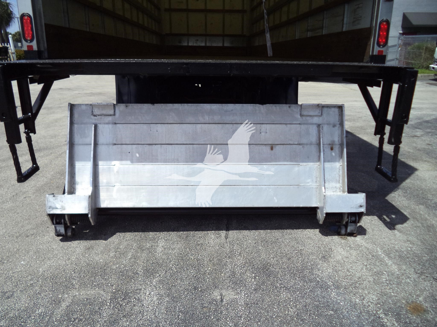 Box truck rear showing a metal tailgate with a white eagle graphic and support arms extending upward, underbody hitch area visible.
