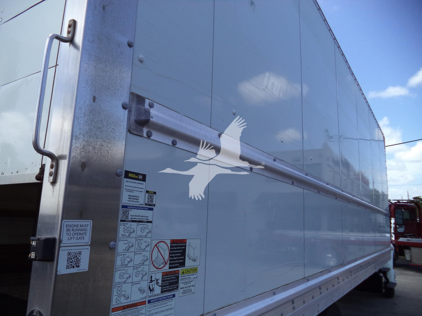 Box truck side showing warning labels and decals, with a large white bird logo on the silver exterior.