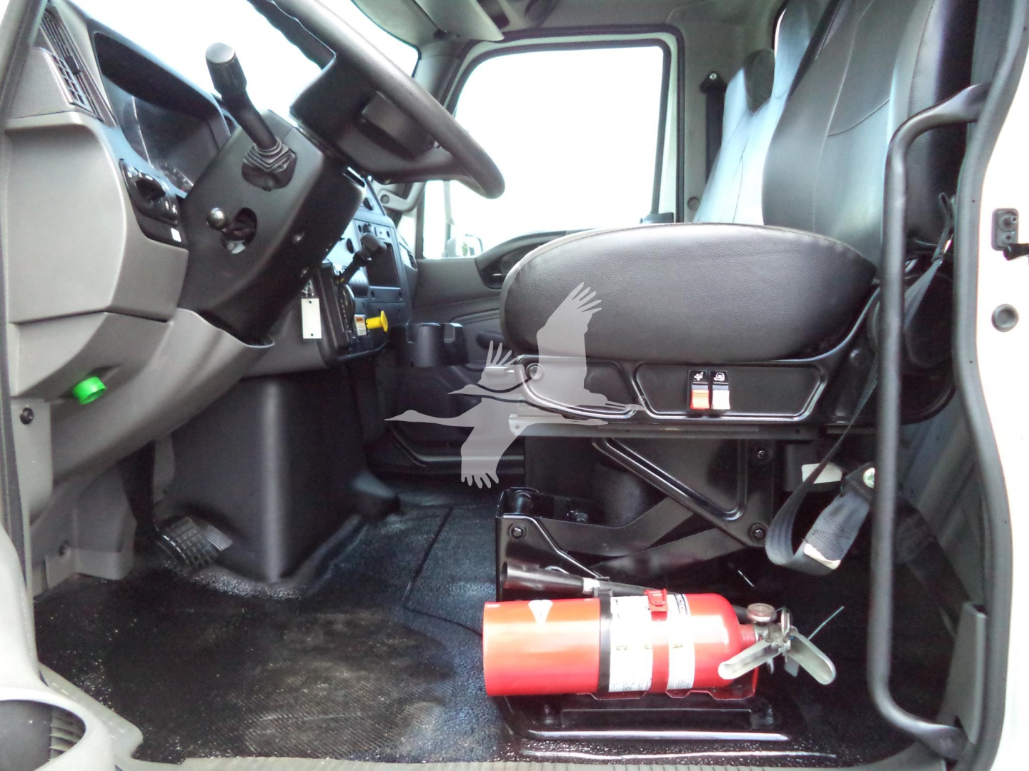 Cab interior of a 2021 International MV truck showing driver's seat, steering wheel, and a mounted fire extinguisher under the seat.