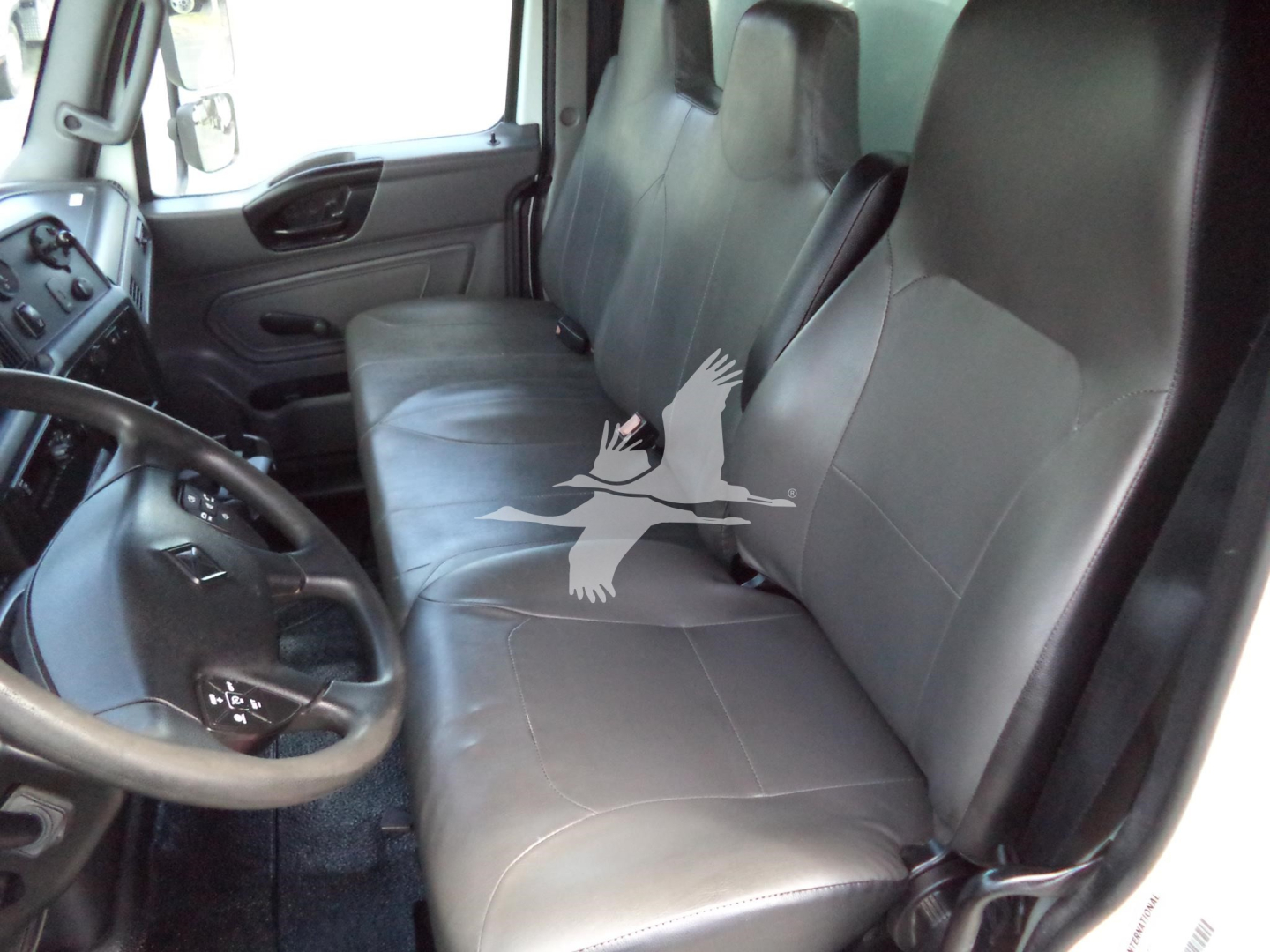 Vehicle cabin interior showing front bench-style seat, steering wheel, and driver's side door panel. Text shows no visible labels beyond the generic components.
