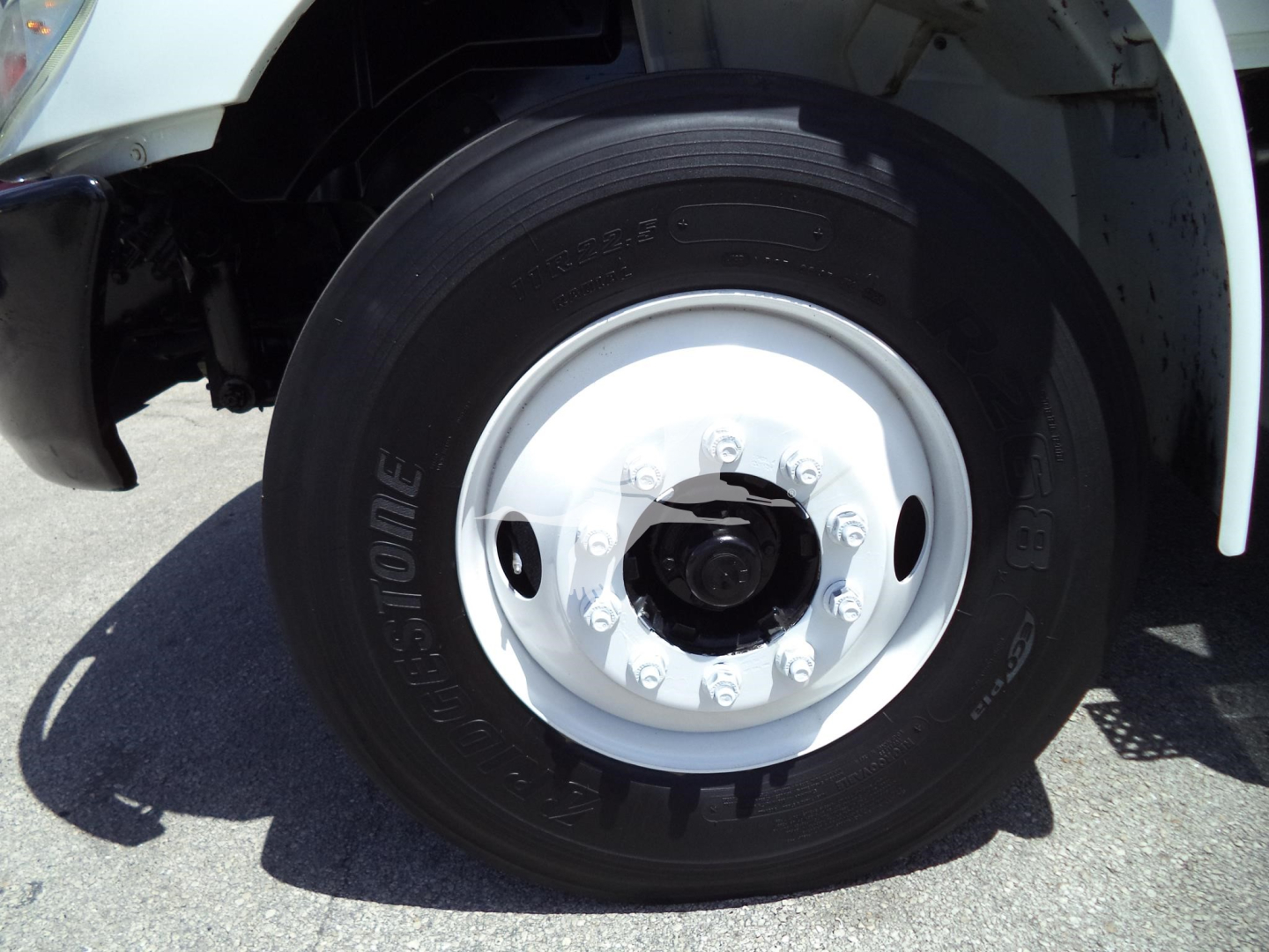 Truck front wheel showing Bridgestone tire and white steel wheel with lug nuts; part of the fender and wheel well visible.