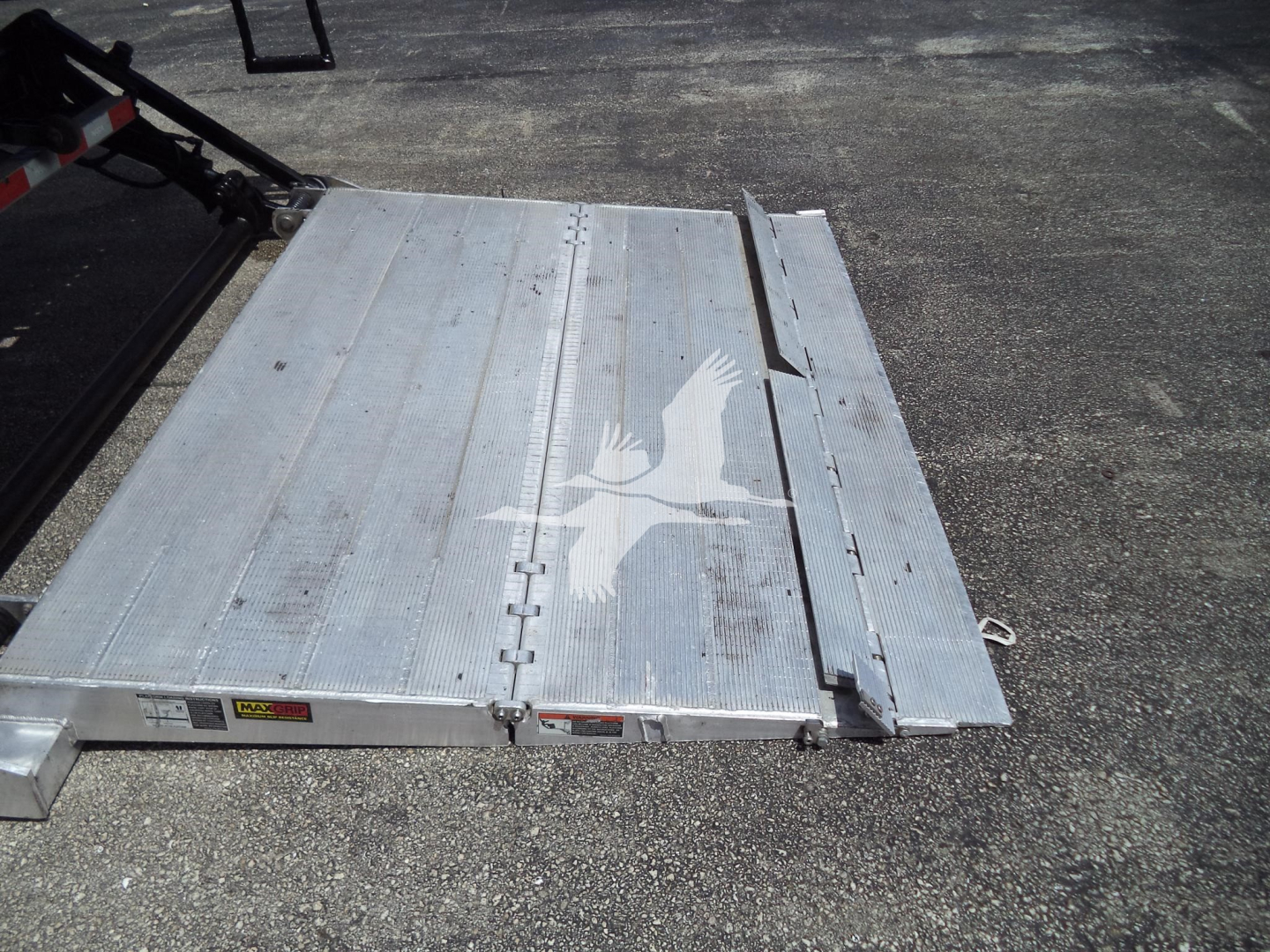 Flatbed truck body with metal platform featuring a white bird graphic and hinges; part of a trailer or ramp.