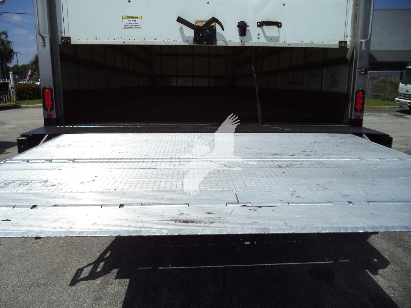 Truck rear with aluminum loading ramp extended from a box truck showing open cargo area.
