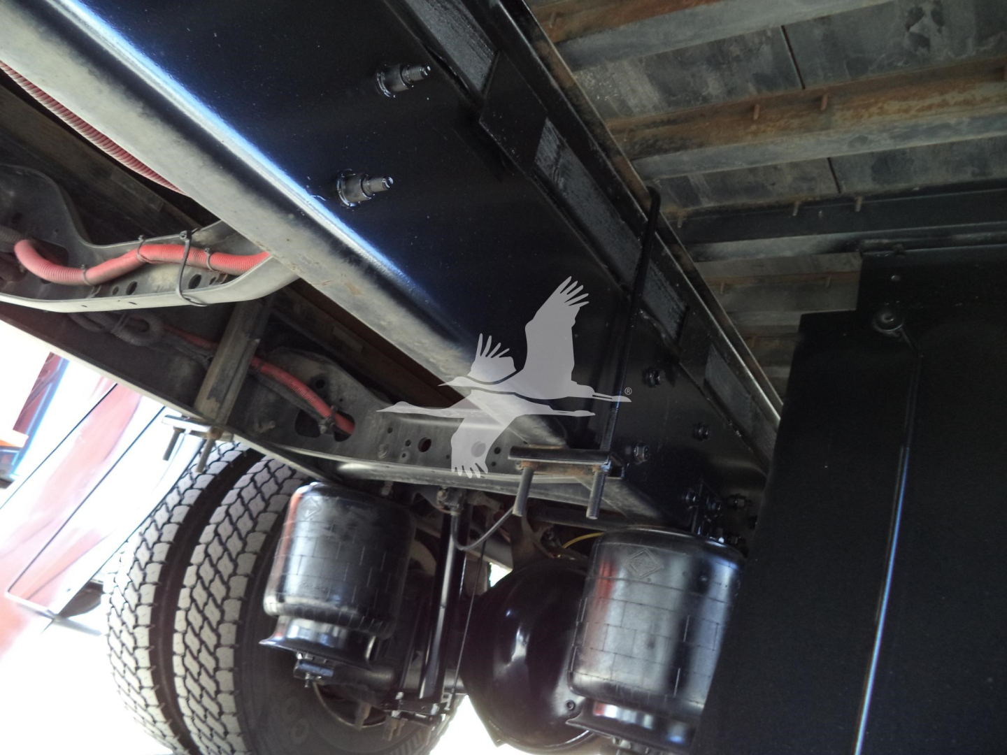 Underbody view of a box truck chassis with dual fuel tanks and wheel, showing undercarriage components and frame.