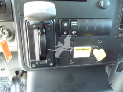 Dashboard area of a 2021 International MV showing controls, ignition switch, and warning label; visible text includes MAKER ROOM? and a yellow warning tag.