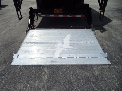 International MV power tailgate/roll-off bed showing aluminum loading ramp and deck with faint bird logo.