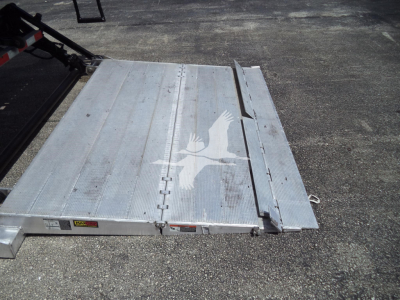 Flatbed truck body with metal platform featuring a white bird graphic and hinges; part of a trailer or ramp.