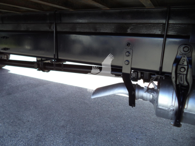 Underbody of a 2021 International MV box truck showing chassis frame, refuse of suspension, and fuel/air lines; visible hardware and a metallic connector at the rear.
