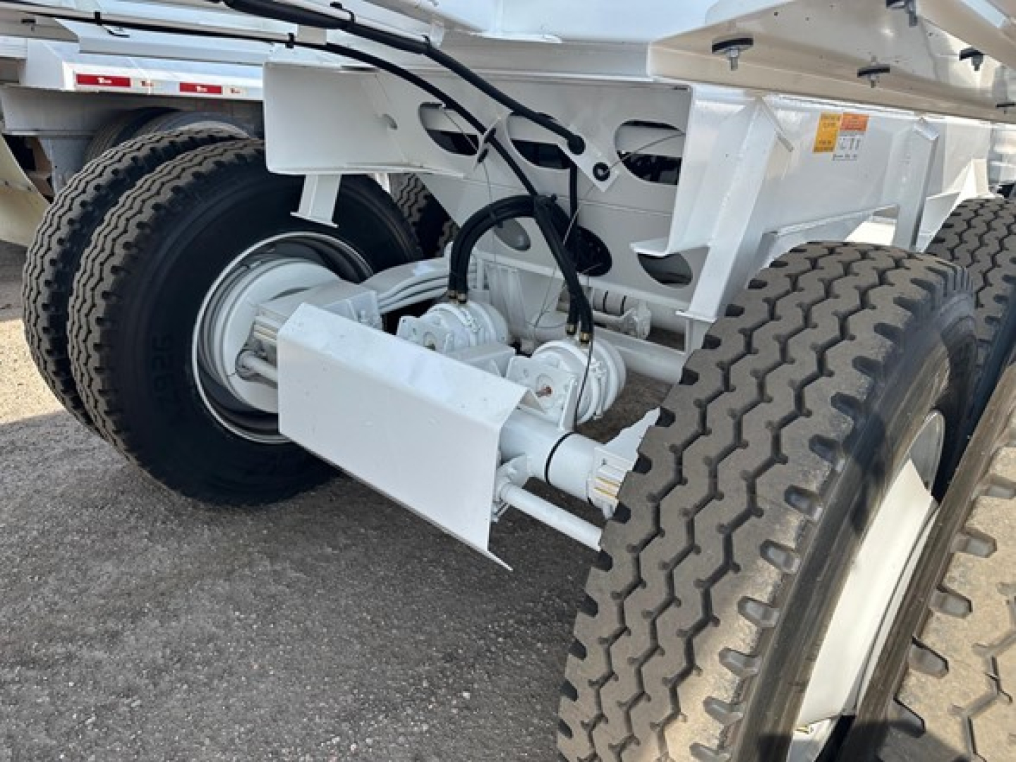 Bottom-dump trailer axle assembly showing dual wheels and hydraulic drive components with white paint and heavy-duty suspension.