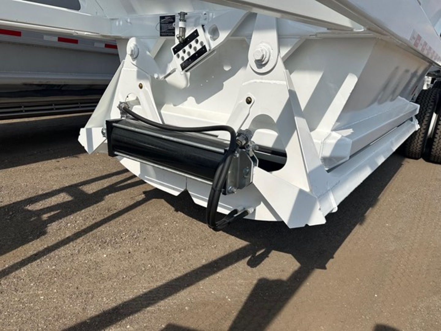 Bottom dump trailer with hydraulic cylinder and frame visible showing white paint and lower hitch area.