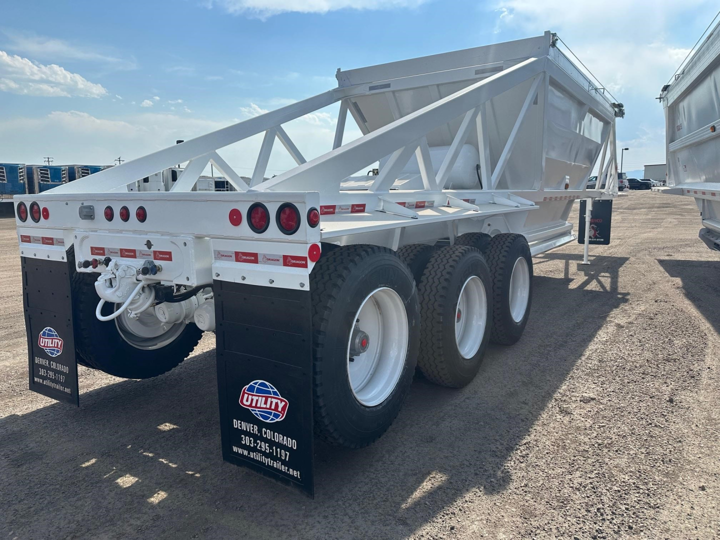 Bottom-dump trailer with three axles and pintle hitch showing rear view and white frame in an outdoor lot.
